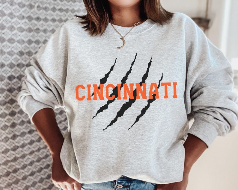 May include: A grey sweatshirt with a black claw mark graphic and the word "CINCINNATI" in orange lettering.