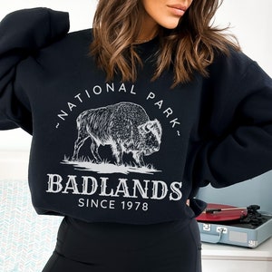May include: Black sweatshirt with a white graphic of a buffalo and the text "National Park" and "Badlands Since 1978".