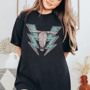 May include: Black oversized t-shirt with a graphic of a skull with horns and lightning bolts in pink, blue, and grey.