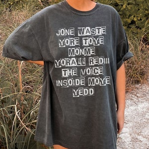 May include: A dark gray t-shirt with a white graphic print of the words "Jone Waste", "Yore Toye", "Monme", "Yore All Red", "The Voice", "Insoide Moye", and "Yedd".