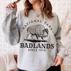 May include: Gray sweatshirt with a black graphic of a bison and the text "Badlands National Park Since 1978".