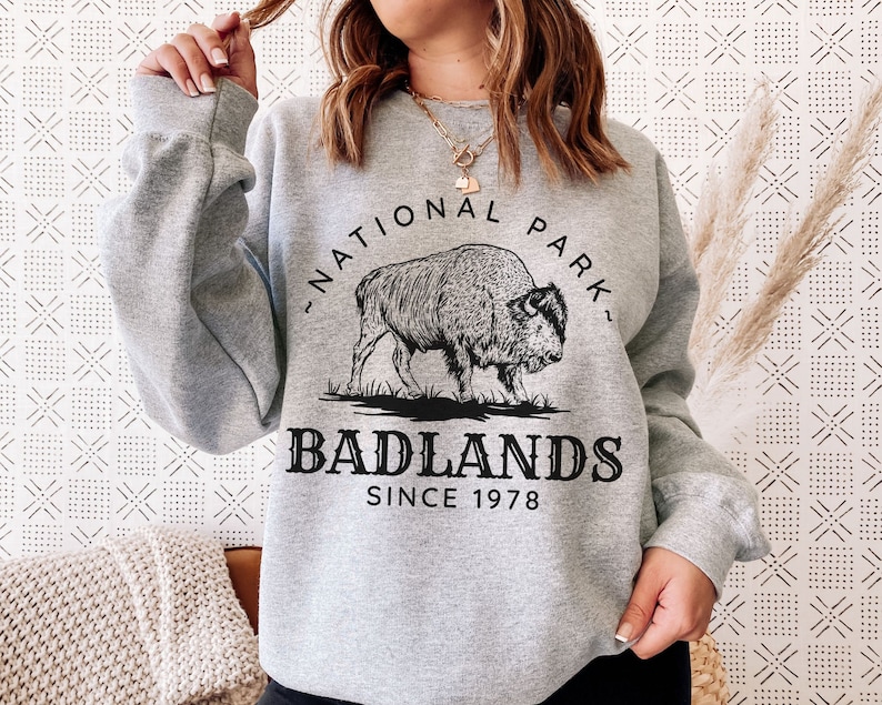 May include: Gray sweatshirt with a black graphic of a bison and the text "Badlands National Park Since 1978".