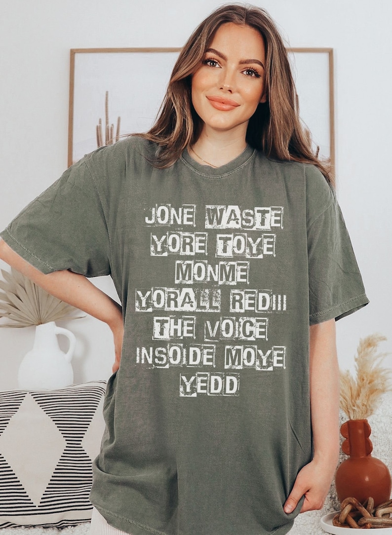 May include: A green t-shirt with a white graphic print that reads "Jone Waste Yore Toye Monme Yore All Redii The Voice Insoide Moye Yedd"