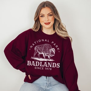 May include: A maroon sweatshirt with a white graphic of a buffalo and the text "National Park" and "Badlands Since 1978".
