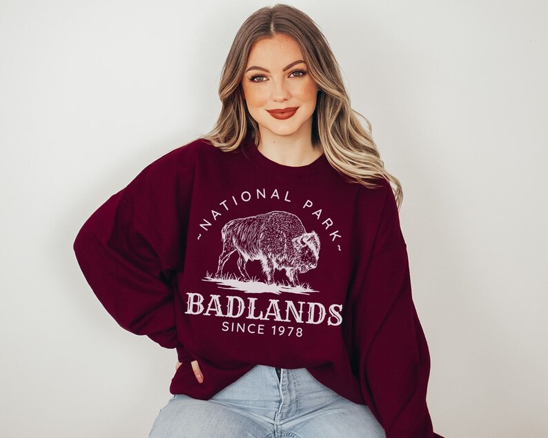May include: A maroon sweatshirt with a white graphic of a buffalo and the text "National Park" and "Badlands Since 1978".
