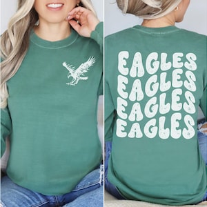 Peut inclure: Un t-shirt &agrave; manches longues vert avec un motif d'aigle blanc sur le devant et le mot "EAGLES" r&eacute;p&eacute;t&eacute; quatre fois dans une police r&eacute;tro au dos.