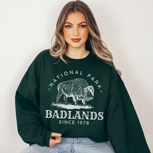 May include: A dark green sweatshirt with a white graphic of a bison and the text "National Park" and "Badlands Since 1978".