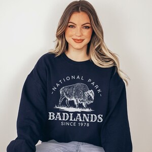 May include: A navy blue sweatshirt with a white graphic of a bison and the text "Badlands National Park - Since 1978".