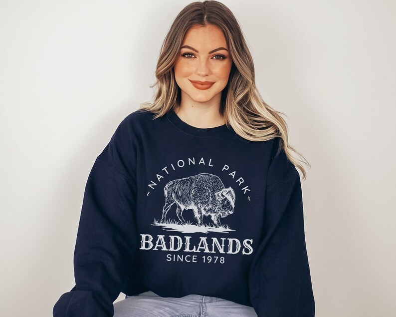 May include: A navy blue sweatshirt with a white graphic of a bison and the text "Badlands National Park - Since 1978".