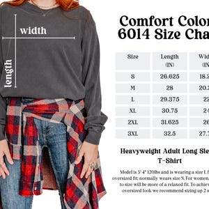 May include: Size chart for Comfort Colors 6014 heavyweight adult long sleeve t-shirt. The chart shows the length and width in inches for sizes S, M, L, XL, 2XL, and 3XL. The model is wearing a size L for an oversized fit.
