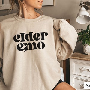 May include: A beige sweatshirt with the text "elder emo" printed in black.