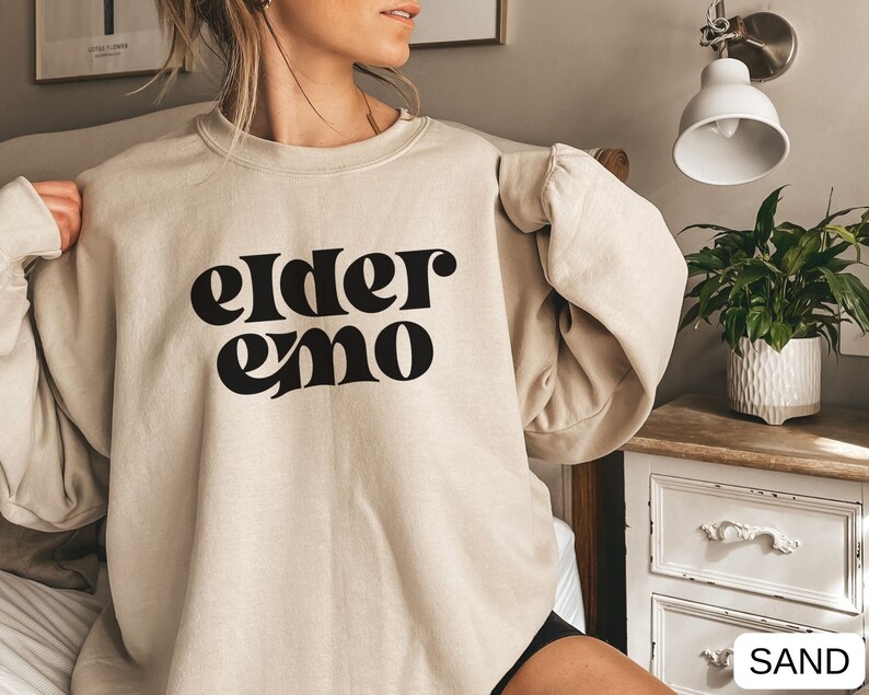 May include: A beige sweatshirt with the text "elder emo" printed in black.