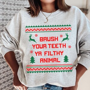 Może przedstawiać: Szara bluza z świątecznym wzorem. Tekst na bluzie brzmi "Brush Your Teeth Ya Filthy Animal".