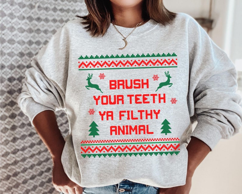 Może przedstawiać: Szara bluza z świątecznym wzorem. Tekst na bluzie brzmi "Brush Your Teeth Ya Filthy Animal".