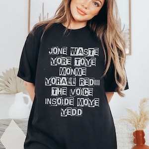 May include: Black t-shirt with white text that reads "Jone Waste Yore Toye Monme Yore All Red III The Voice Inside Moye Yedd"