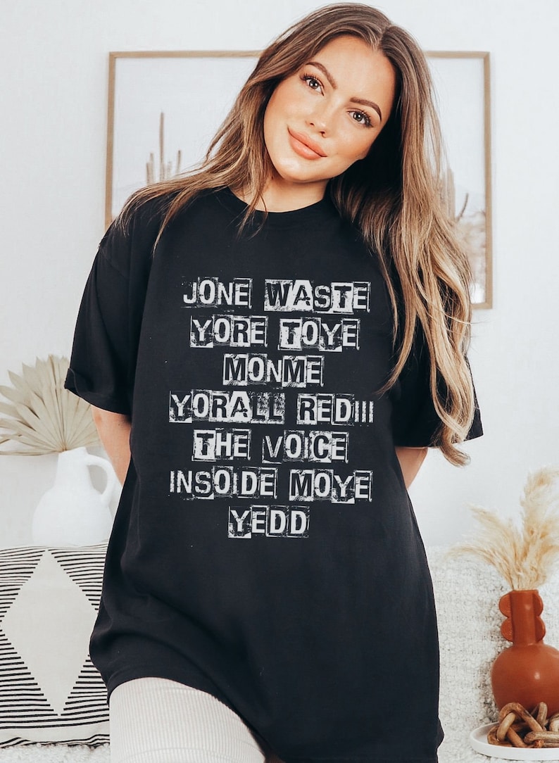 May include: Black t-shirt with white text that reads "Jone Waste Yore Toye Monme Yore All Red III The Voice Inside Moye Yedd"