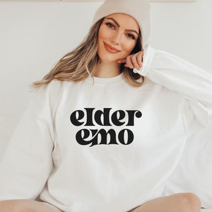 May include: White sweatshirt with black text that reads "elder emo" in a retro font.