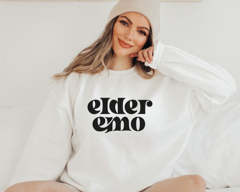 May include: White sweatshirt with black text that reads "elder emo" in a retro font.