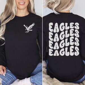 Peut inclure: T-shirt &agrave; manches longues noire avec un graphique d'aigle blanc sur le devant et le mot "EAGLES" r&eacute;p&eacute;t&eacute; dans une police r&eacute;tro au dos.
