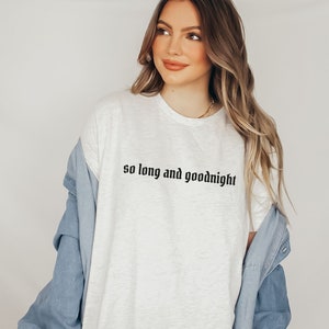 May include: White t-shirt with the text "so long and goodnight" in black lettering. The shirt is being worn by a person with long blonde hair and a denim jacket.
