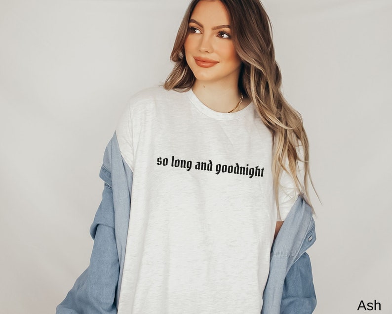 May include: White t-shirt with the text "so long and goodnight" in black lettering. The shirt is being worn by a person with long blonde hair and a denim jacket.