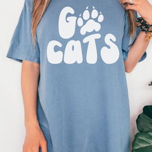 May include: A blue jean t-shirt with a white graphic that says "Go Cats" with a paw print in the "O".