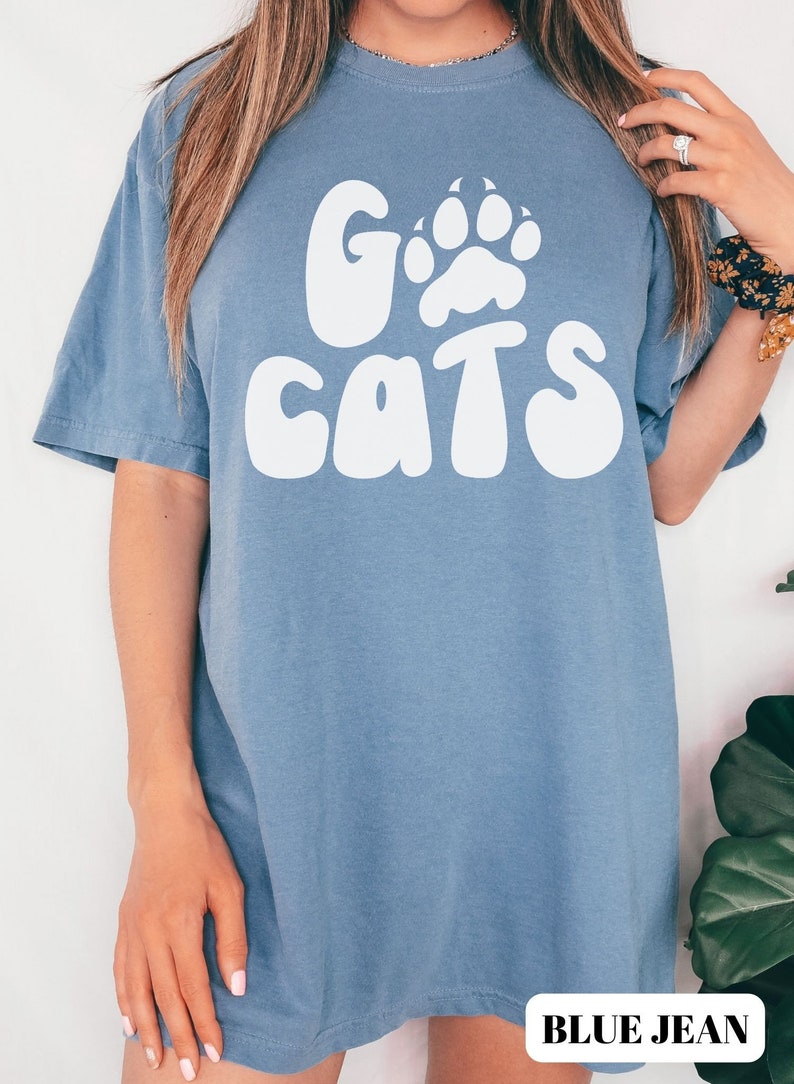 May include: A blue jean t-shirt with a white graphic that says "Go Cats" with a paw print in the "O".