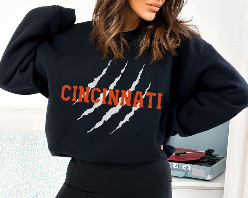 May include: Black sweatshirt with a white claw mark graphic and the word "CINCINNATI" in orange text.