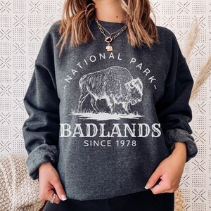 May include: A dark gray sweatshirt with a white graphic of a buffalo and the text "National Park - Badlands - Since 1978".