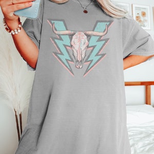 May include: A gray oversized t-shirt with a graphic of a pink and white bull skull with turquoise lightning bolts behind it.