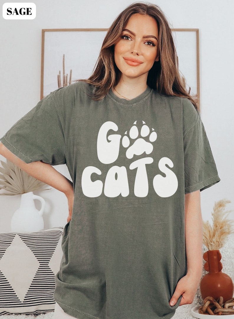 May include: Sage green t-shirt with a white graphic that says "Go Cats" with a paw print in the "O".