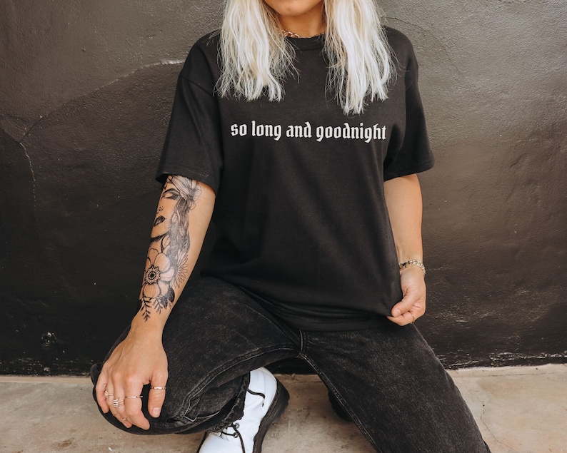 May include: A black t-shirt with the text "so long and goodnight" in white lettering. The person wearing the shirt has a floral tattoo on their arm.