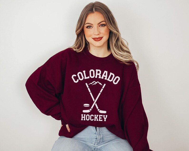 May include: A maroon sweatshirt with a white graphic design featuring the text "COLORADO HOCKEY" and a pair of crossed hockey sticks with a puck at the bottom.