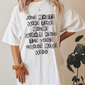 May include: White oversized t-shirt with black text that reads "Jone Waste Yore Toye Monme Yore All Red!! The Voice Insode Moye Yedd"