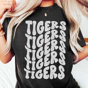 Peut inclure: Un t-shirt noir avec un motif graphique blanc du mot "TIGERS" r&eacute;p&eacute;t&eacute; en forme de vague.
