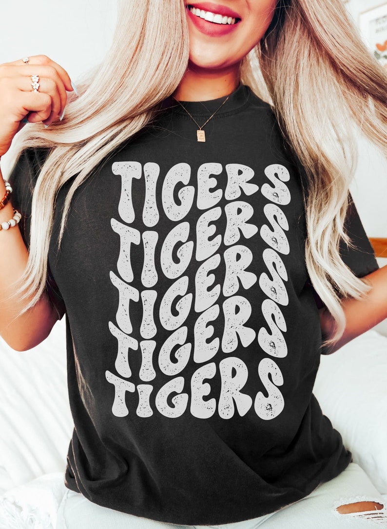 Peut inclure: Un t-shirt noir avec un motif graphique blanc du mot "TIGERS" r&eacute;p&eacute;t&eacute; en forme de vague.