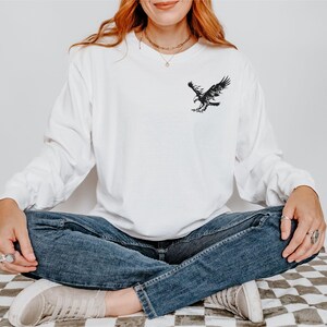Peut inclure: Un t-shirt blanc &agrave; manches longues avec un motif d'aigle noir sur la poitrine gauche.