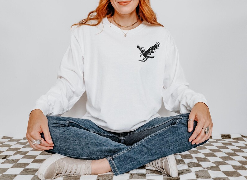 Peut inclure: Un t-shirt blanc &agrave; manches longues avec un motif d'aigle noir sur la poitrine gauche.