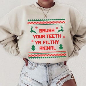 Może przedstawiać: Beżowa bluza z czerwono-zielonym wzorem świątecznym. Tekst na bluzie brzmi "Brush your teeth ya filthy animal".
