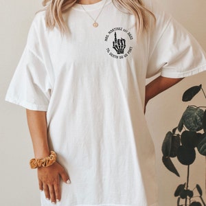 Op de afbeelding: Wit oversized T-shirt met een zwarte afbeelding van een skelet hand die de middelvinger opsteekt. De afbeelding bevindt zich in een cirkel met de tekst "Mrs. Martinez Est. 2023 Til Death Do Us Part".