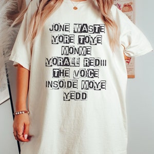May include: White t-shirt with black text that reads "Jone Waste Yore Toye Monme Yore All Red!! The Voice Inside Moye Yedd"