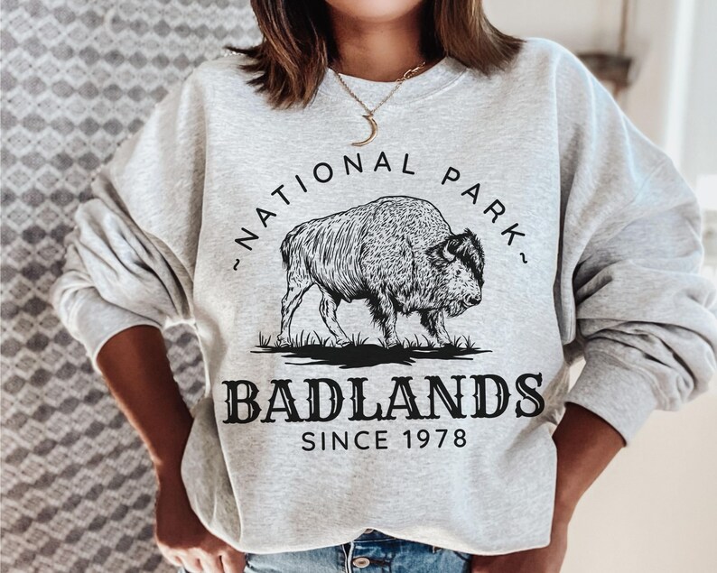 May include: Gray sweatshirt with a black and white graphic of a bison and the text "National Park" and "Badlands Since 1978".
