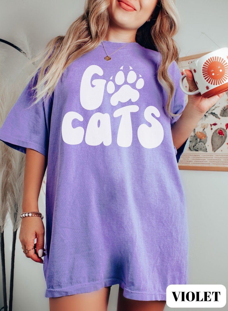 May include: A purple t-shirt with a white graphic that says "Go Cats" with a paw print in the "O".