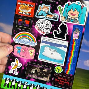 Op de afbeelding: Een stickervel met diverse illustraties in internet-meme-thema, waaronder een kat die keyboard speelt, een regenboog, een bananenfiguur en een Club Penguin-tutorial. Het vel heeft een zwarte achtergrond met roze glitters en tekst.