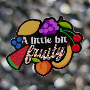 May include: A black and white sticker with a glittery rainbow design that says "A little bit fruity". The sticker features a variety of fruits including a lemon, grapes, a watermelon, a peach, a banana, and cherries.
