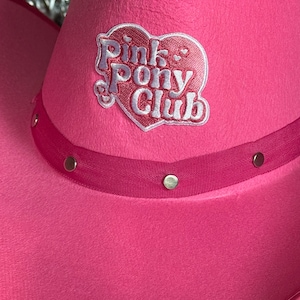 May include: Pink cowboy hat with a pink heart-shaped patch that says "Pink Pony Club" in white lettering.