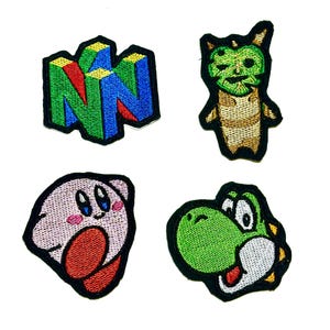 May include: Four embroidered patches featuring video game characters and logos. Includes a green, blue, and yellow N64 logo, a green creature, a pink Kirby, and a green Yoshi with a white belly.