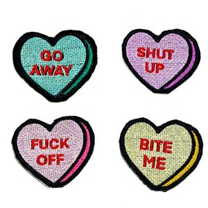 Puede incluir: Cuatro parches bordados en forma de corazón con frases descaradas. Los parches presentan las frases "GO AWAY", "SHUT UP", "FUCK OFF" y "BITE ME" en texto rojo. Cada parche tiene una combinación de colores diferente, incluyendo turquesa, lavanda, rosa y amarillo.