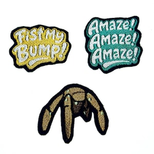 Può includere: Tre toppe ricamate su sfondo bianco. Una dice "FIST MY BUMP!" in giallo e bianco su bordo nero. Un'altra dice "Amaze! Amaze! Amaze!" in bianco e verde acqua. La terza toppa è un ragno marrone.