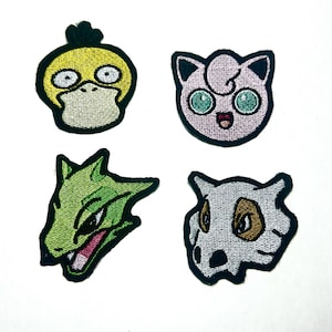 May include: Four embroidered patches featuring cartoon character heads. One is a yellow duck-like creature, one is a pink round creature with large green eyes, one is a green reptilian creature, and one is a grey skull-like creature with brown eyes.